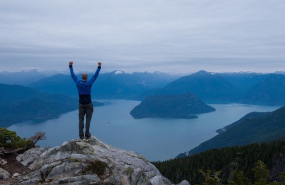 Un homme levant les bras devant des fjords. 