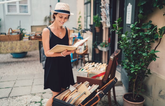 Jeune femme souriante en robe noire lisant un livre devant une librairie en plein air.
