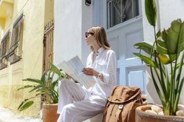 Personne assise sur les marches d’une maison, consultant une carte de voyage, avec un sac à dos posé à côté.