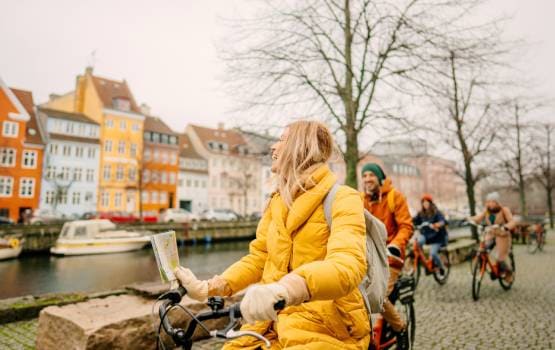 Personnes circulant à vélo le long d’un canal bordé de maisons colorées dans un centre-ville européen.