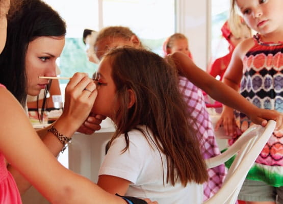 Une jeune femme est en train de maquiller des petites filles