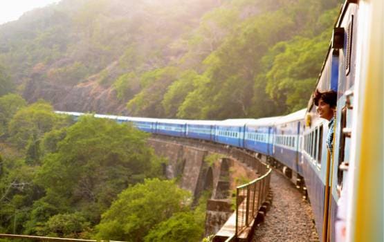Train de voyageurs traversant un viaduc au cœur d’une vallée verdoyante entourée de collines boisées.