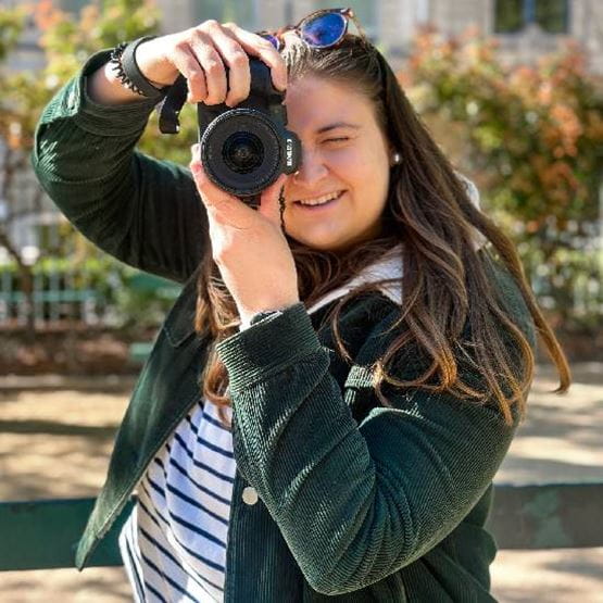 Une fille brune prenant une photo avec un apparail devant son oeil. 