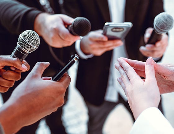 Plusieurs journalistes tendent leurs micros pour capter les paroles de la présentatrice