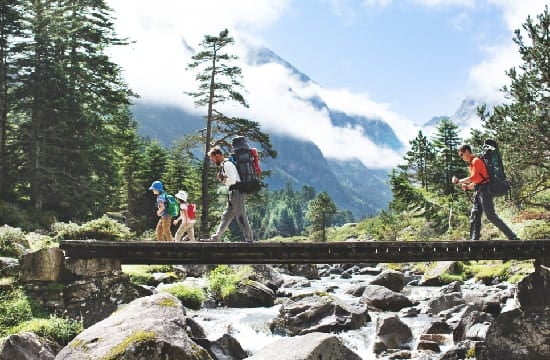 Une famille traversant un rondin de bois en guise de pont en pleine montagne.