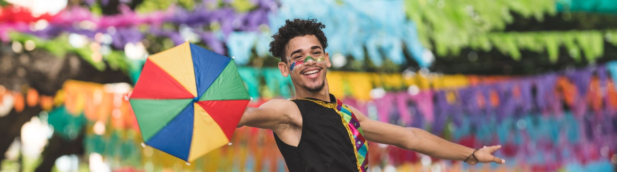 1 homme déguisé en costumes colorés célébrant un carnaval en riant sous le soleil.