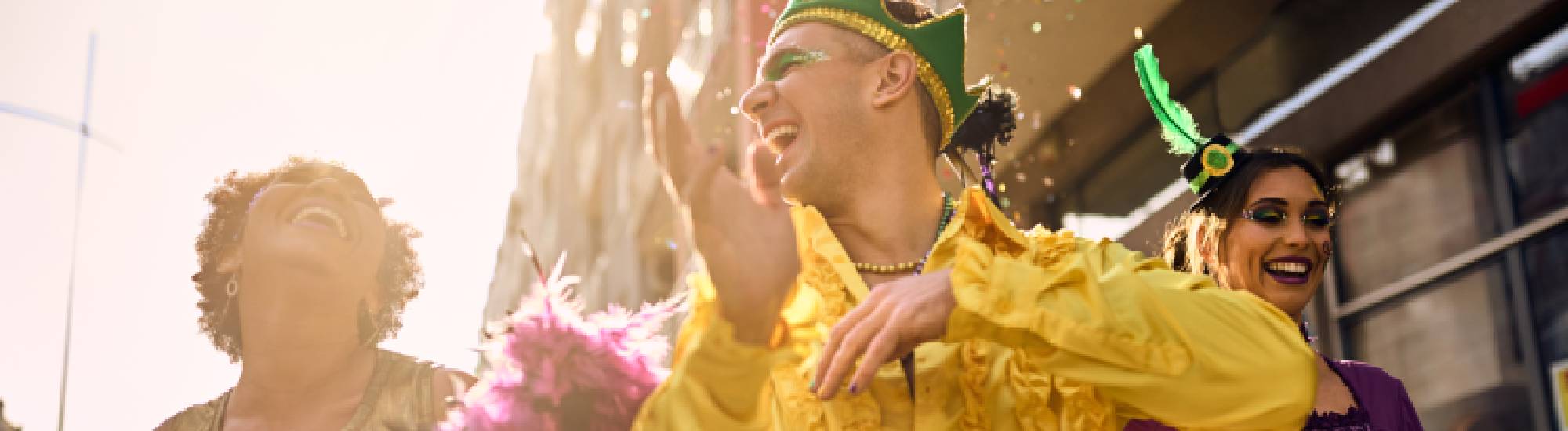 Groupe de personnes déguisées en costumes colorés célébrant un carnaval en riant sous le soleil.