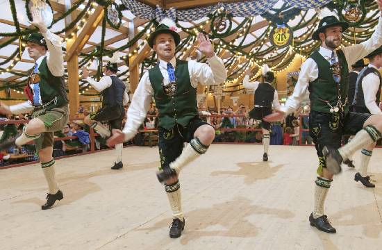 Groupe d’hommes en costume bavarois traditionnel dansant pendant l’Oktoberfest dans une grande tente décorée.