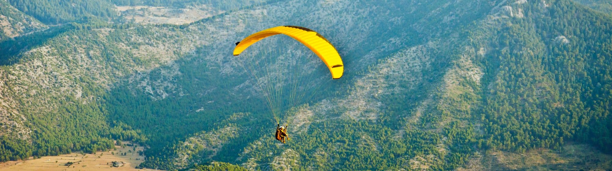 Un homme faisant du parachute au milieu des montagnes face à un coucher de soleil. 
