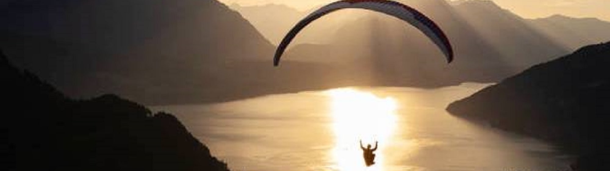 Un homme faisant du parachute au milieu des montagnes face à un coucher de soleil. 