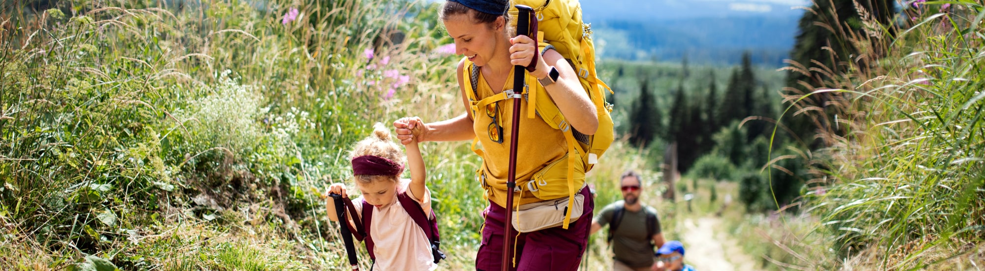 Une maman aidant sa fille sur un chemin de randonnée en pleine montagne. 