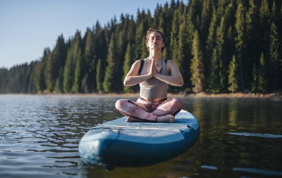 Une femme réalise une pause assise sur son padel sur un lac. 