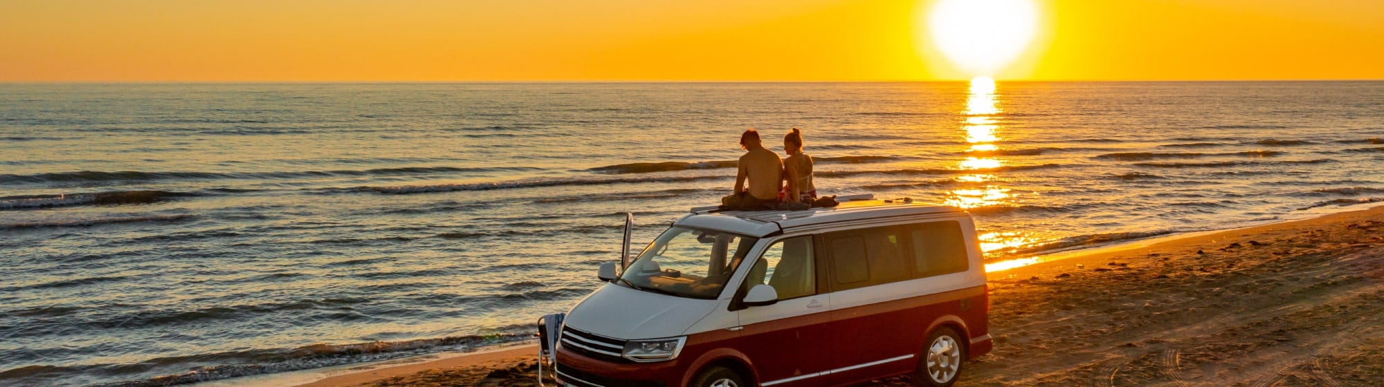 Van posé sur une plage devant coucher de soleil. 