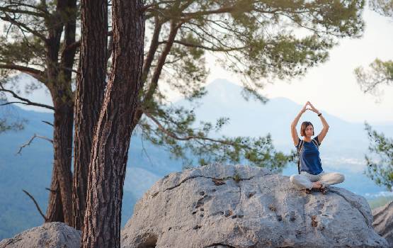 Une dame réalise une pause de yoga sur un rocher face aux montagnes. 