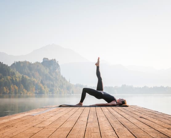 Une dame réalise une pause de yoga sur un rocher face aux montagnes.