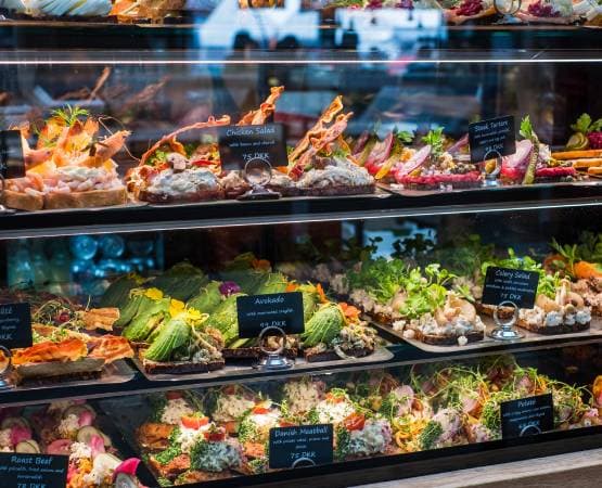 Vitrine de traiteur avec salades composées, poissons et plats frais présentés en étagères.