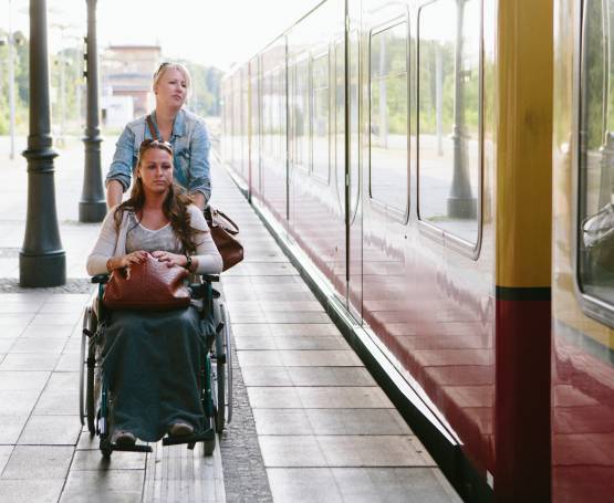 Une femme en fauteuil roulant sur le quai d'une gare à côté d'un train