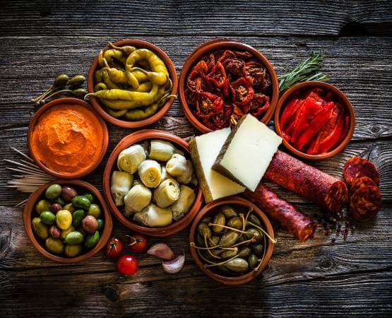 Assortiment de tapas espagnoles avec olives, fromages, charcuterie et légumes marinés.